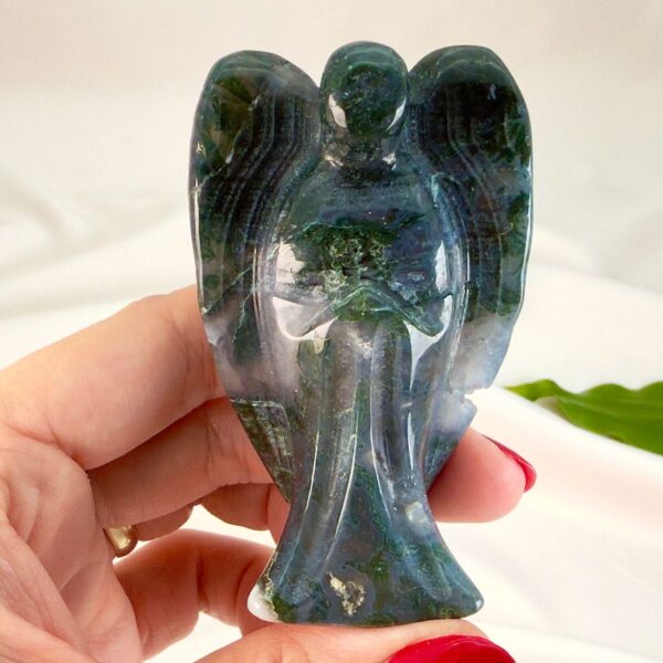 Agat mos krystal engel mellem fingre på hvid baggrund med grønt blad