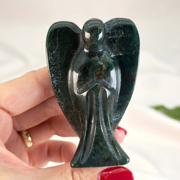 Agat mos krystal engel mellem fingre på hvid baggrund med grønt blad med tags