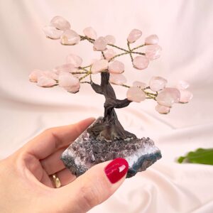 Rosakvarts træ på krystal bund i hånd med lys baggrund og grønt blad