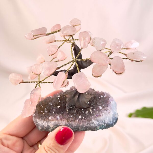 Rosakvarts træ på krystal bund i hånd med lys baggrund og grønt blad