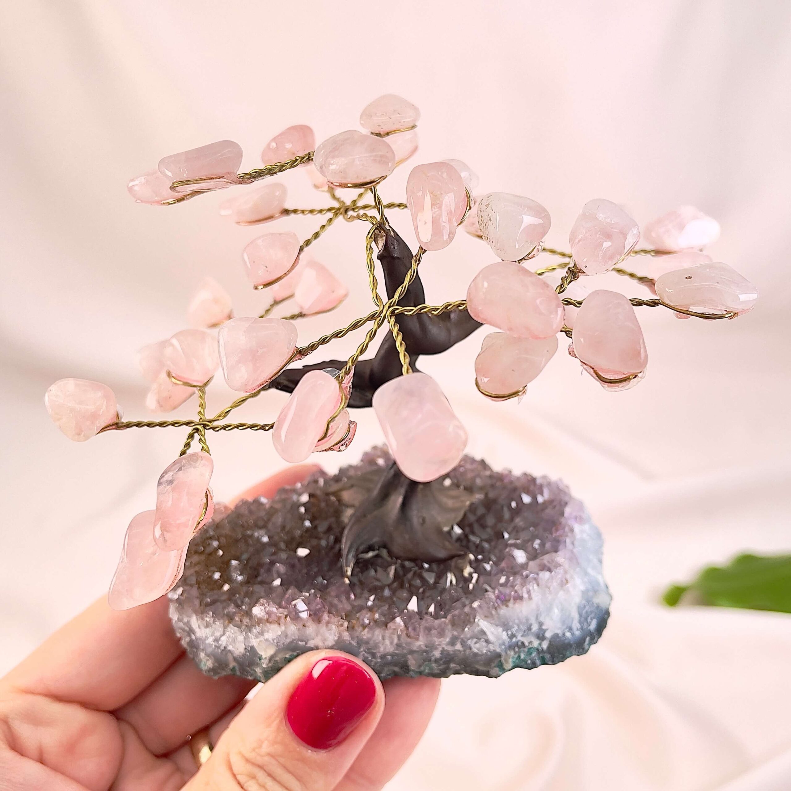 Rosakvarts træ på krystal bund i hånd med lys baggrund og grønt blad