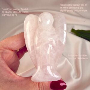 Rosakvarts krystal engel mellem fingre på hvid baggrund med grønt blad og tags