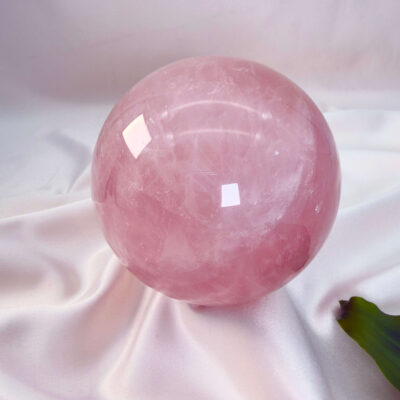 Rosakvarts krystal kugle på hvid baggrund med grønt blad