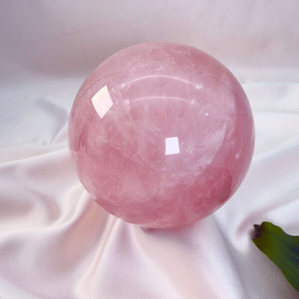 Rosakvarts krystal kugle på hvid baggrund med grønt blad