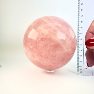 Rosakvarts krystal kugle ved siden af lineal på hvid baggrund