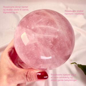 Rosakvarts krystal kugle imellem fingre på hvid baggrund med grønt blad med tags
