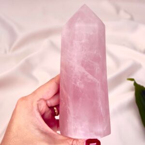 Rosakvarts krystal tårn mellem fingre med hvid baggrund og grønt blad
