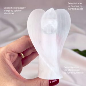 Selenit krystal engel imellem fingre på hvid baggrund med grønt blad og tags