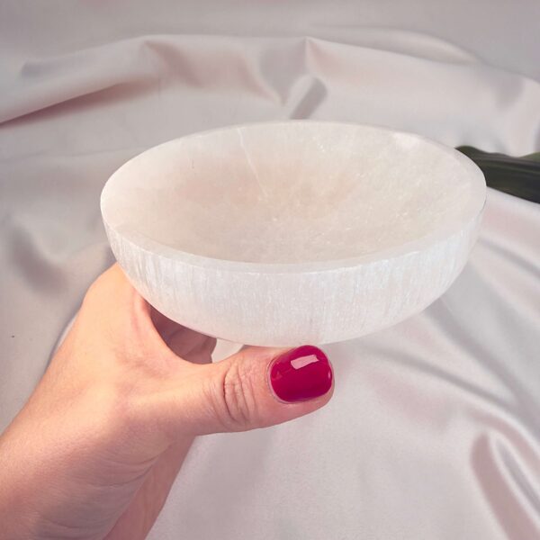 Selenit krystal 12 cm skål mellem fingre på hvid baggrund med grønt blad