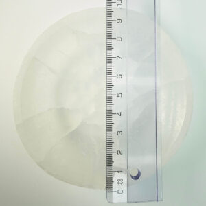 Selenit krystal 9,5 cm skål med lineal liggende ovenpå på hvid plade med blå baggrund