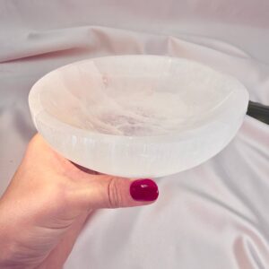 Selenit krystal 14 cm skål mellem fingre på hvid baggrund med grønt blad