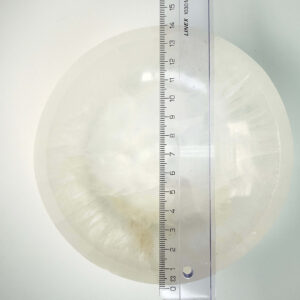 Selenit krystal 14 cm skål med lineal liggende ovenpå på hvid plade med blå baggrund