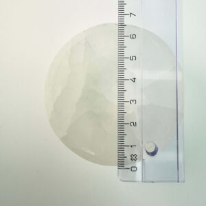 Selenit krystal 6,5 cm skål med lineal liggende ovenpå på hvid plade med blå baggrund