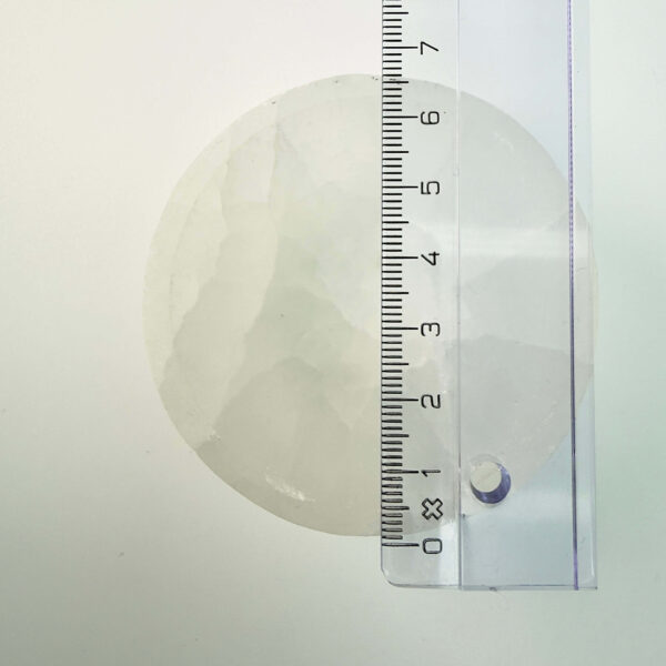 Selenit krystal 6,5 cm skål med lineal liggende ovenpå på hvid plade med blå baggrund