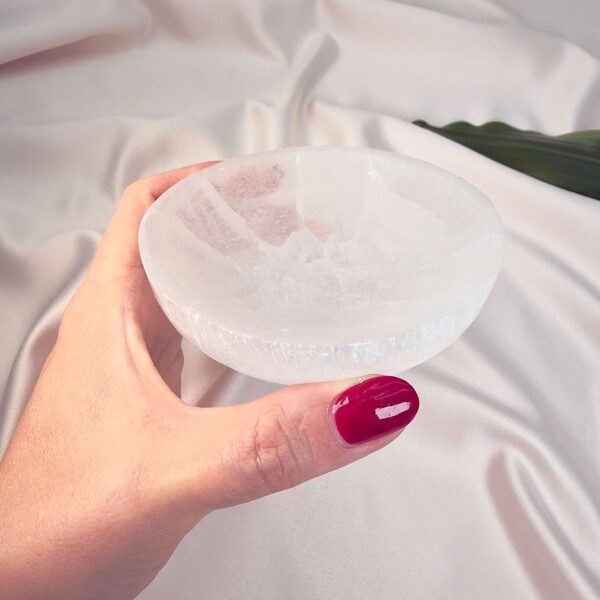 Selenit krystal 9,5 cm skål mellem fingre på hvid baggrund med grønt blad