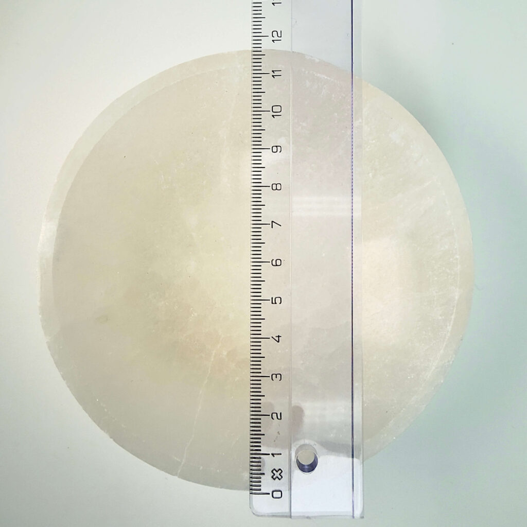 Selenit krystal 12 cm skål med lineal liggende ovenpå på hvid plade med blå baggrund