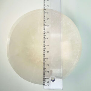 Selenit krystal 12 cm skål med lineal liggende ovenpå på hvid plade med blå baggrund