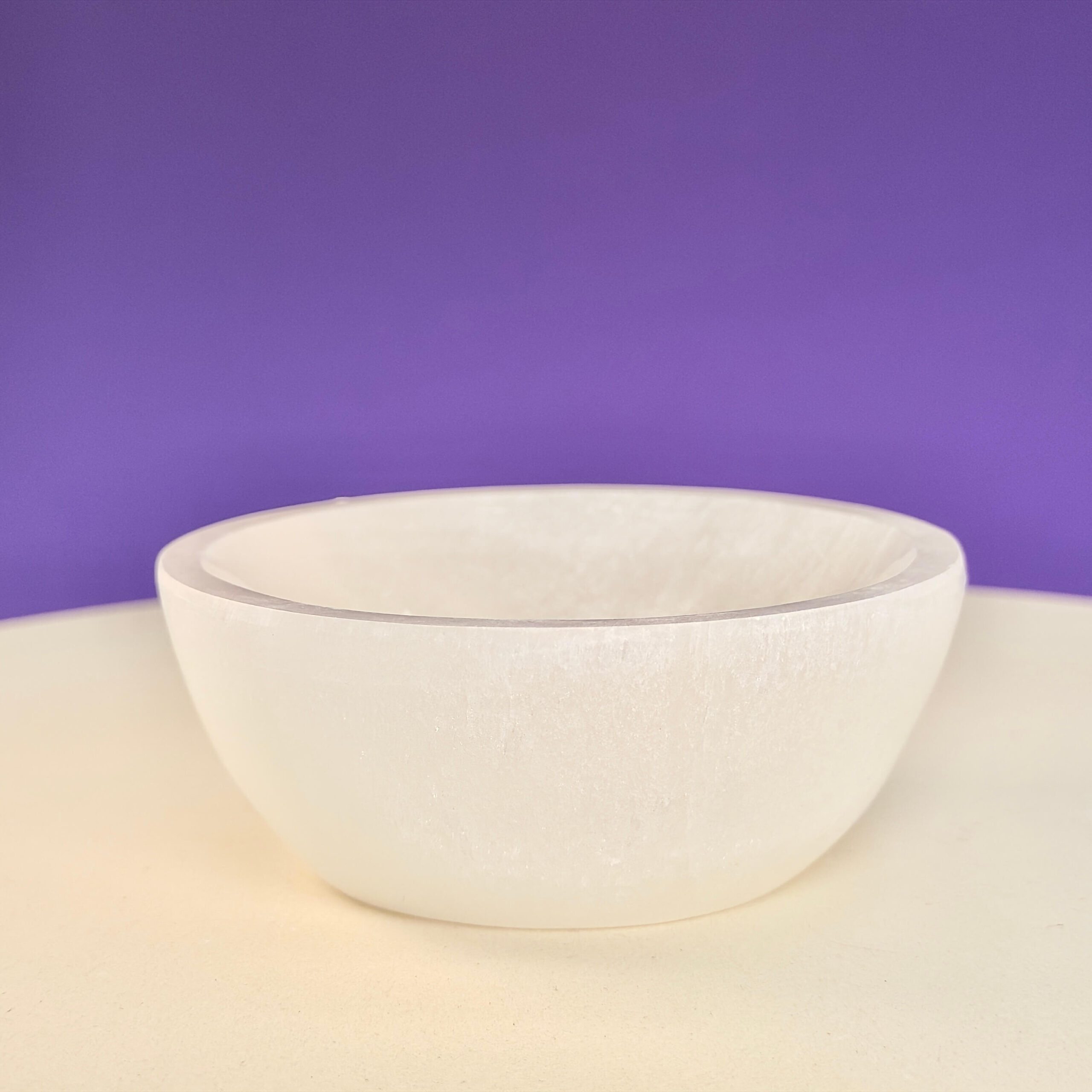 Selenit skål krystal sten 10 cm på hvid plade med lilla baggrund