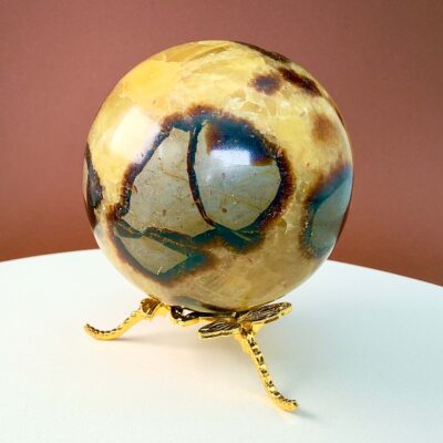 Septarie krystal kugle på guldholder på hvid plade med brun baggrund