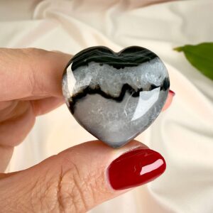 Sort agat krystal hjerte mellem fingre på hvid baggrund med blad