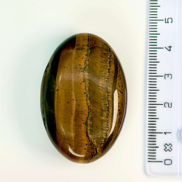 Tigerøje krystal håndsten ved siden af lineal på hvid baggrund