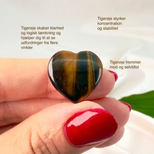 Tigerøje mini krystal hjerte mellem fingre med hvid baggrund og grønt blad og med tags