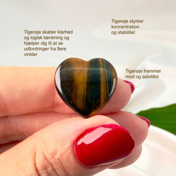 Tigerøje mini krystal hjerte mellem fingre med hvid baggrund og grønt blad og med tags