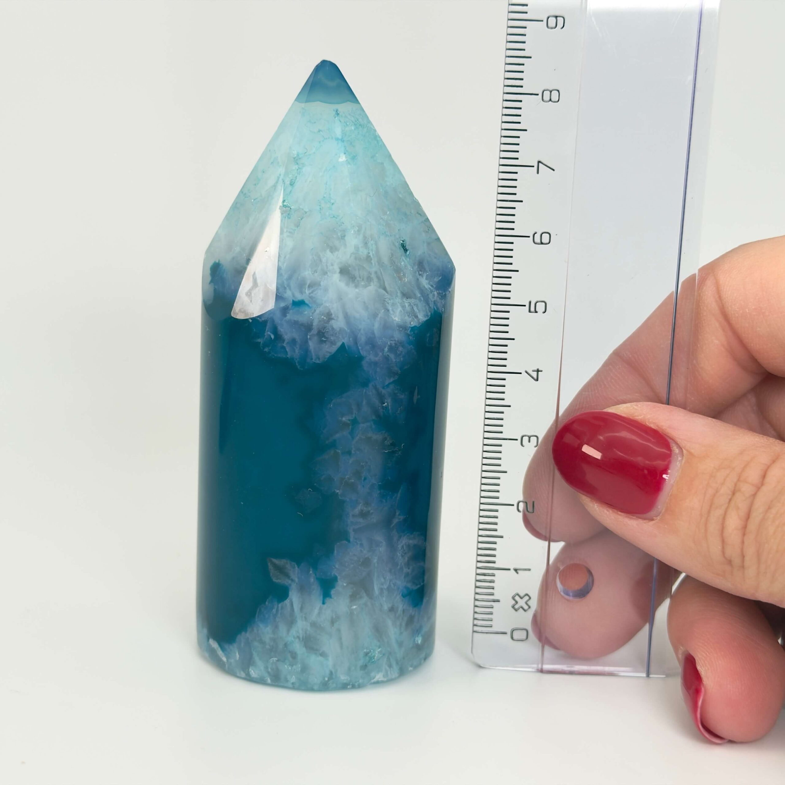 Agat blå krystal spids sten i hånd med lineal på hvid baggrund
