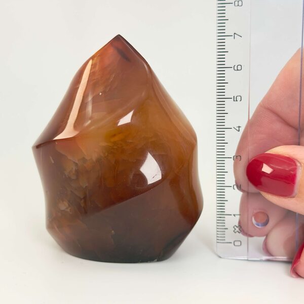 Karneol Freeform Flamme krystal sten med lienal og hånd på hvid baggrund