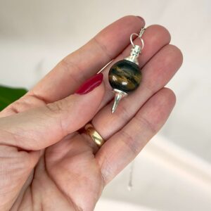 Tigerøje Pendul Krystal Sten med kæde i hånd på hvid baggrund