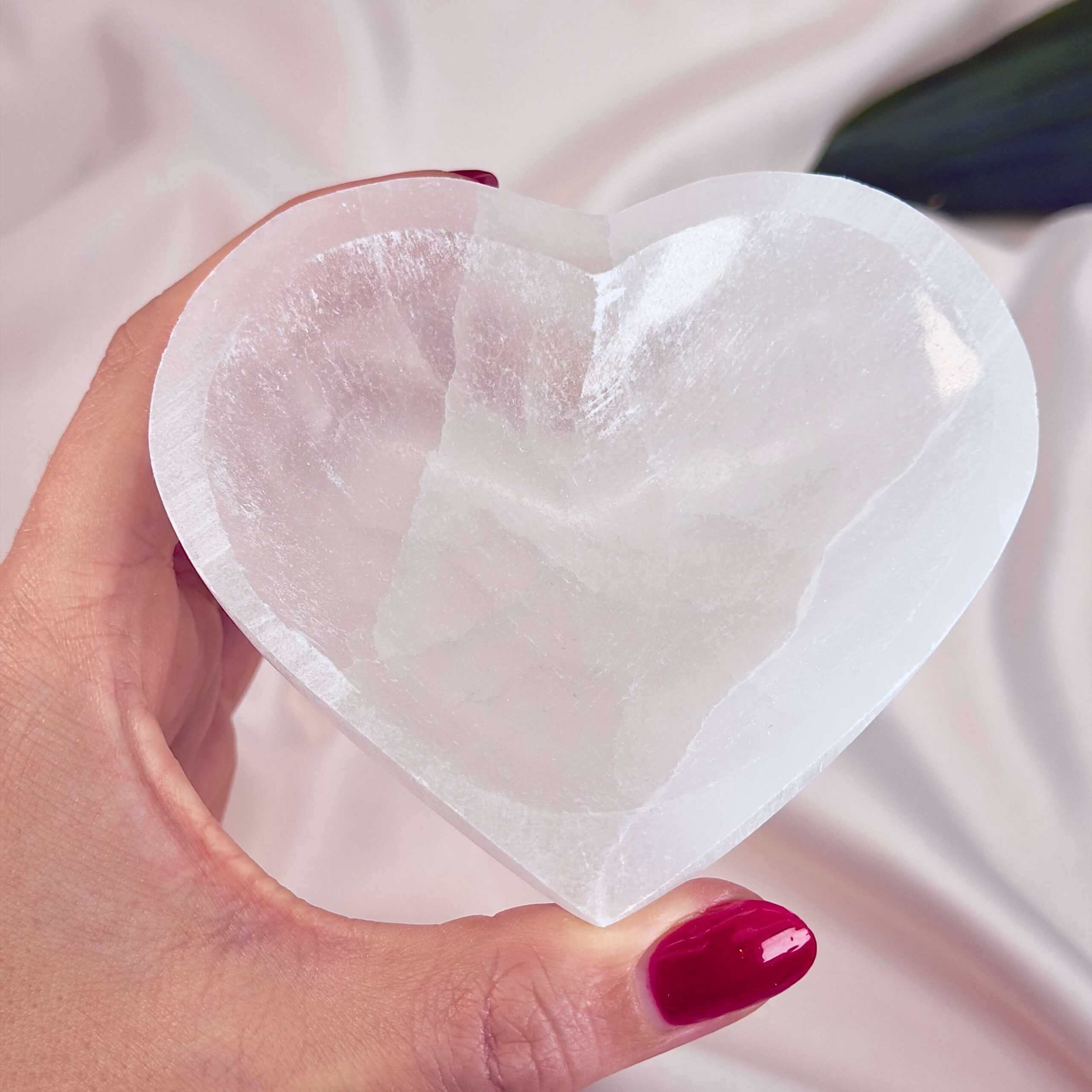 Selenit hjerte skål krystal sten 10 cm i hånd på hvid baggrund