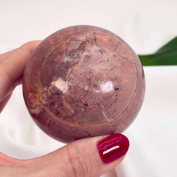 Jordbær Calsit Kugle Krystal Sten i hånd på hvid baggrund