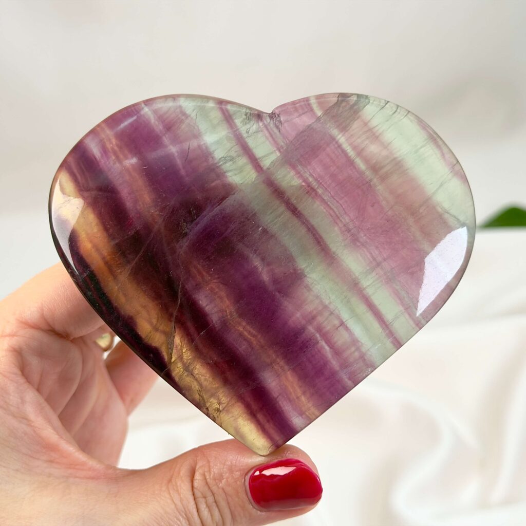 Ametyst vs. Fluorit 2 Fluorit Regnbue Hjerte Krystal Sten med hånd på hvid baggrund