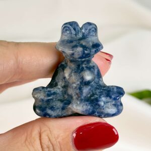 Krystal meditationsfrø 4 cm sodalit mellem fingre på hvid baggrund