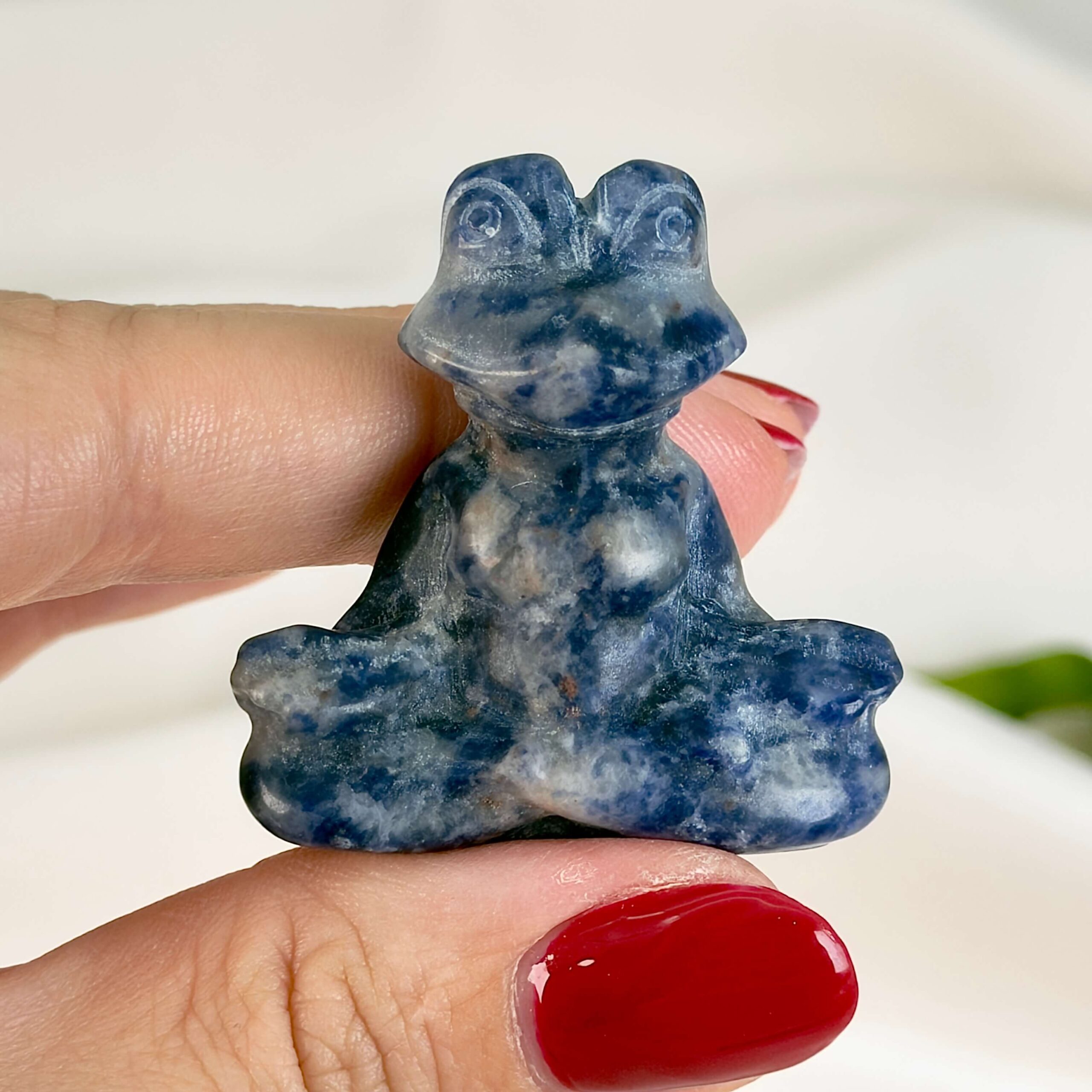 Krystal meditationsfrø 4 cm sodalit mellem fingre på hvid baggrund