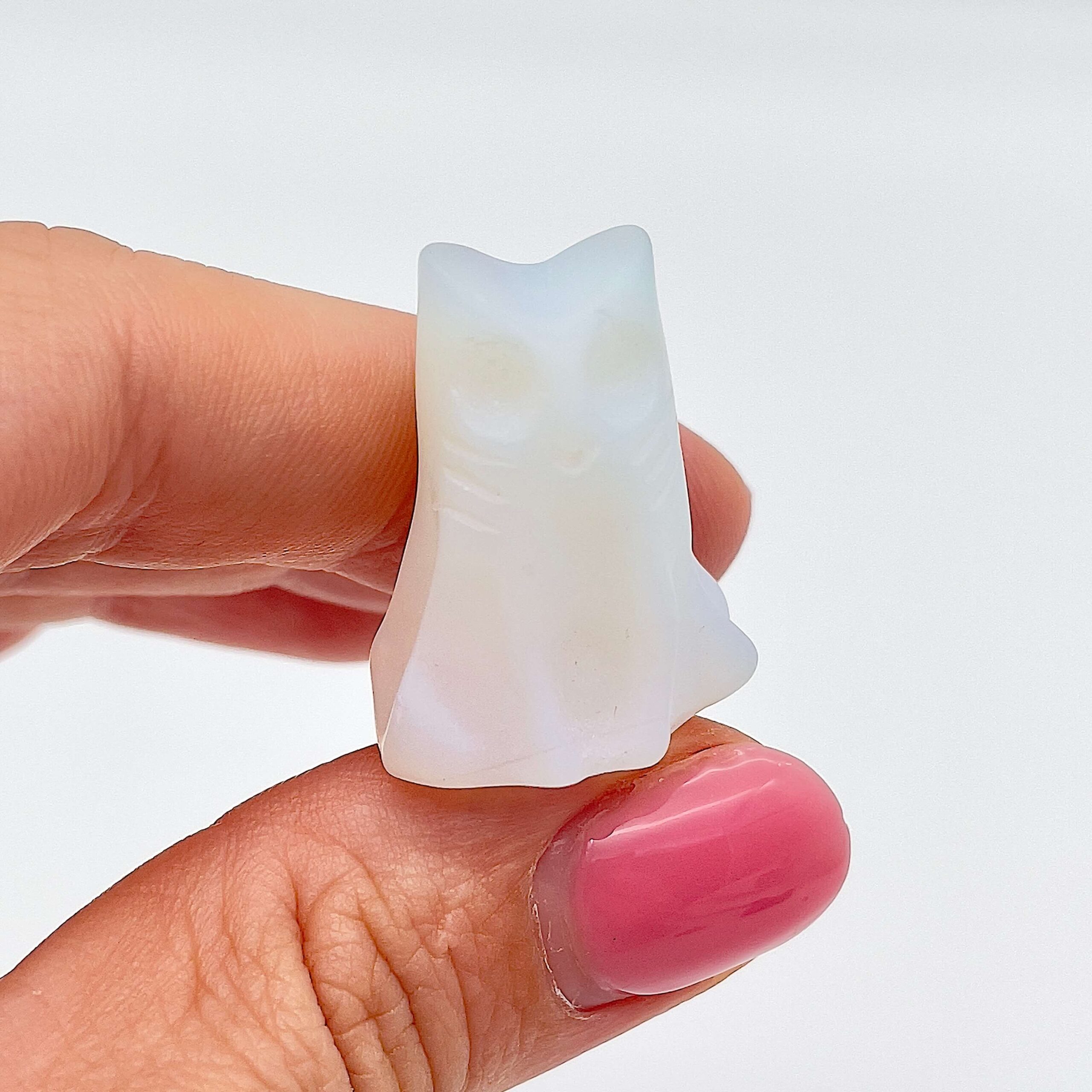 Sten krystal spøgelseskat 3 cm opalit mellem fingre på hvid baggrund