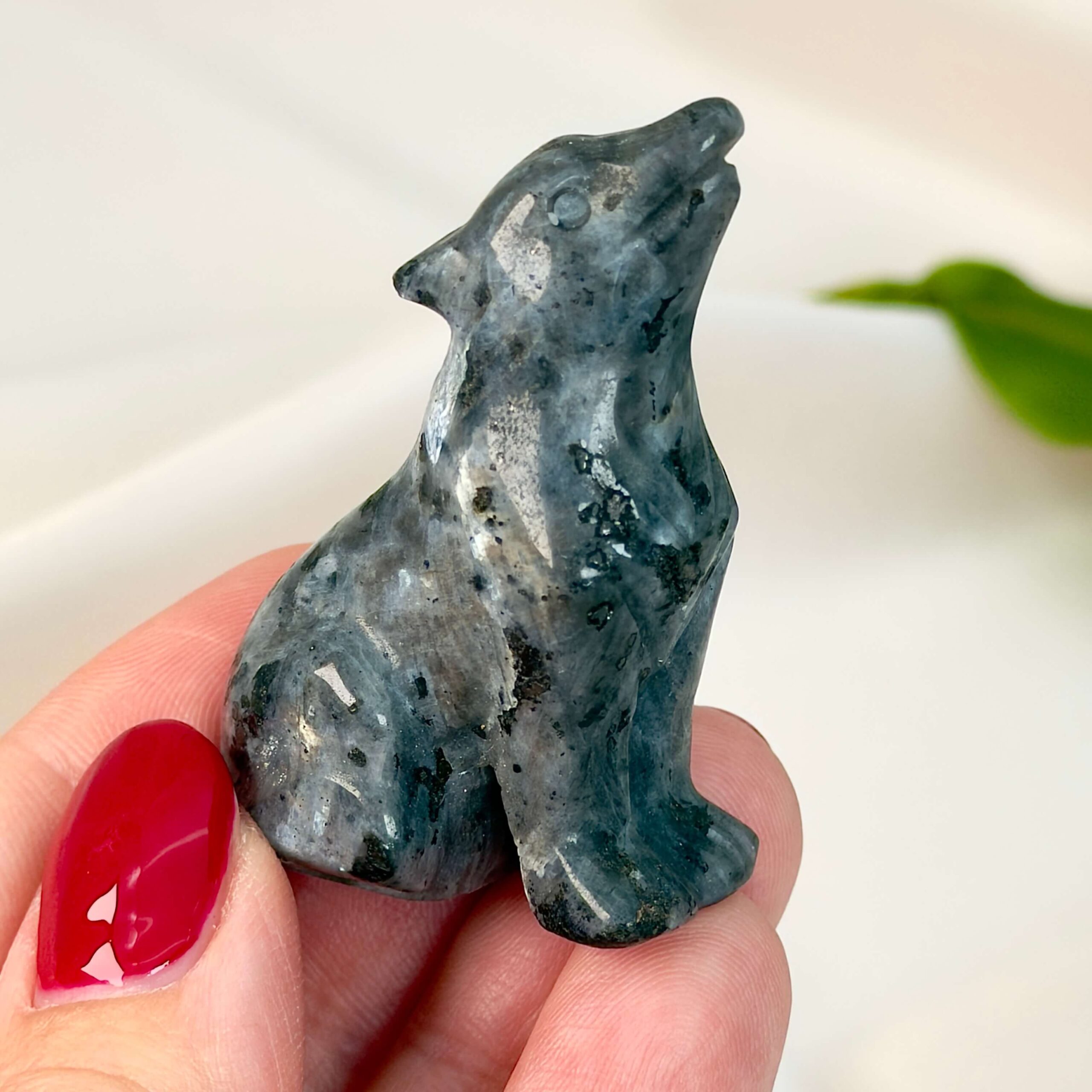 Sten krystal ulv 5 cm larvikit imellem fingre på hvid baggrund med grønt blad