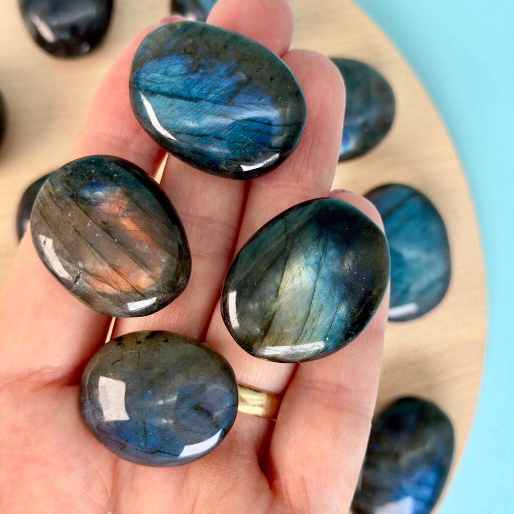 Krystaller mod stress 4 Labradorit Premium Lommesten Krystal Sten I hånd på træ og blå baggrund