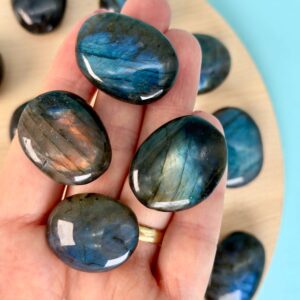 Labradorit Premium Lommesten Krystal Sten I hånd på træ og blå baggrund