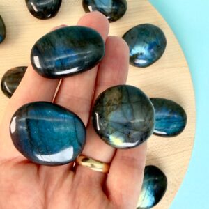 Labradorit Premium Lommesten Krystal Sten I hånd på træ og blå baggrund