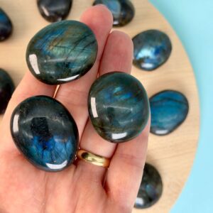 Labradorit Premium Lommesten Krystal Sten I hånd på træ og blå baggrund