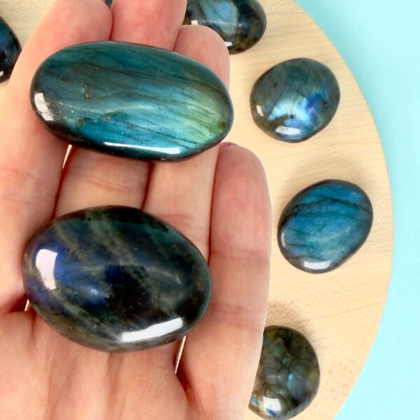 Labradorit Premium Lommesten Krystal Sten I hånd på træ og blå baggrund