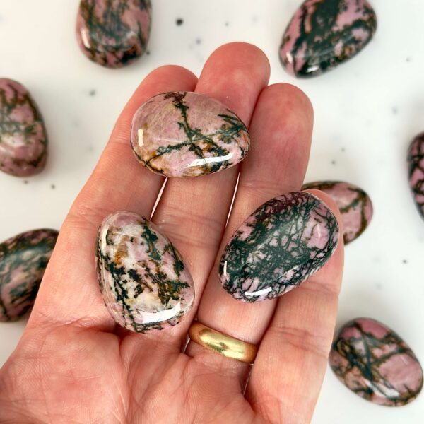 Rhodonit dråbe premium lommesten krystal sten i hånd på hvid baggrund