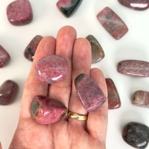 Rhodonit lommesten krystal sten i hånd på hvid baggrund