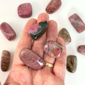 Rhodonit lommesten krystal sten i hånd på hvid baggrund