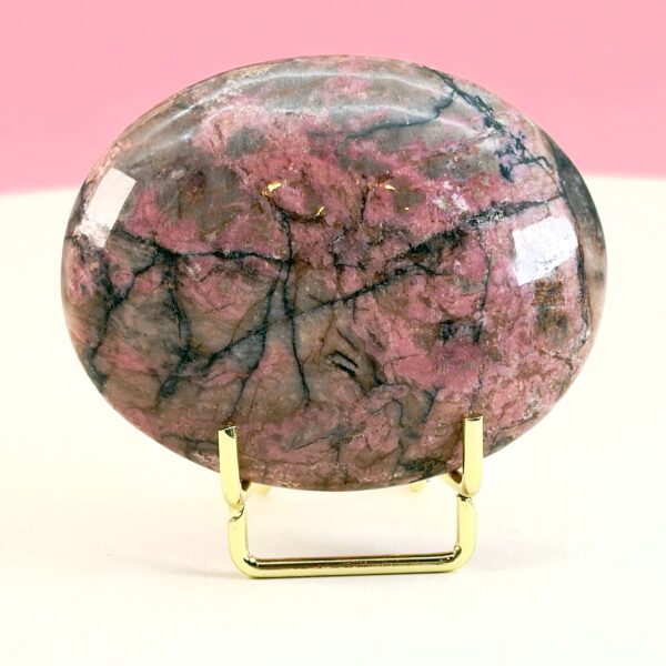 Rhodonit håndsten krystal sten i holder på hvid plade med lyserød baggrund