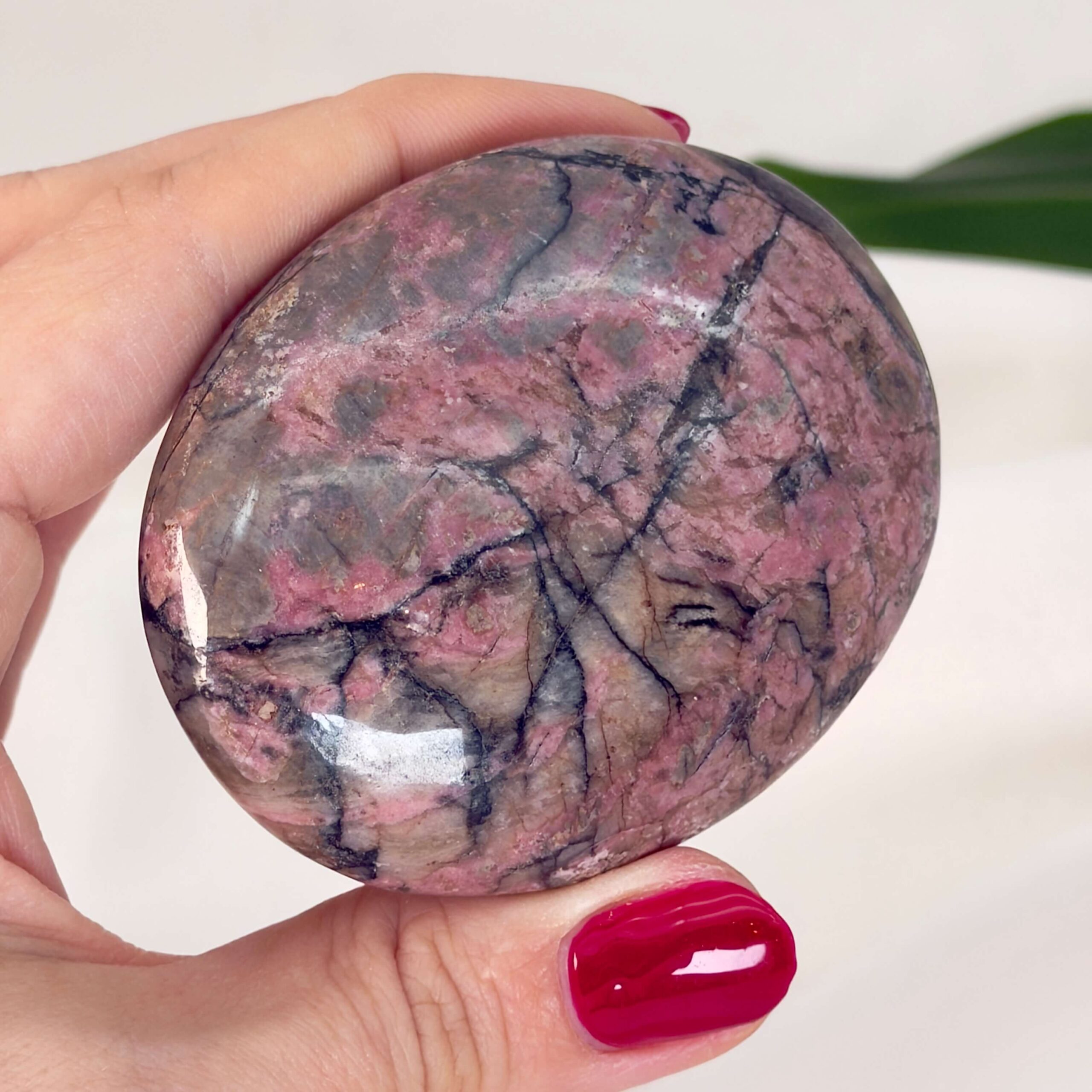 Rhodonit håndsten krystal sten i hånd med hvid baggrund