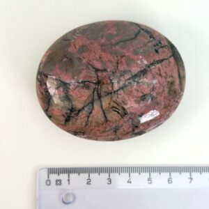 Rhodonit håndsten krystal sten ved siden af lineal på hvid baggrund