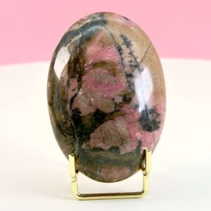 Rhodonit håndsten krystal sten i holder på hvid plade med lyserød baggrund