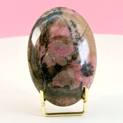 Rhodonit håndsten krystal sten i holder på hvid plade med lyserød baggrund